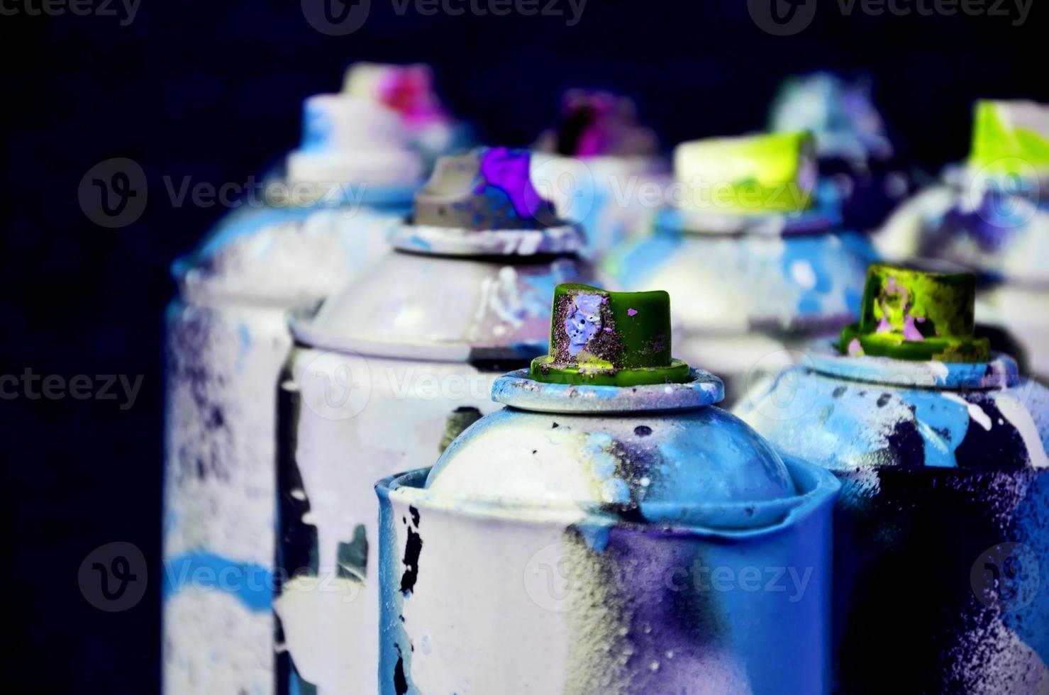 Still life with a large number of used colorful spray cans of aerosol paint lying on the treated wooden surface in the artist's graffiti workshop. Dirty and stained cans for spray art photo