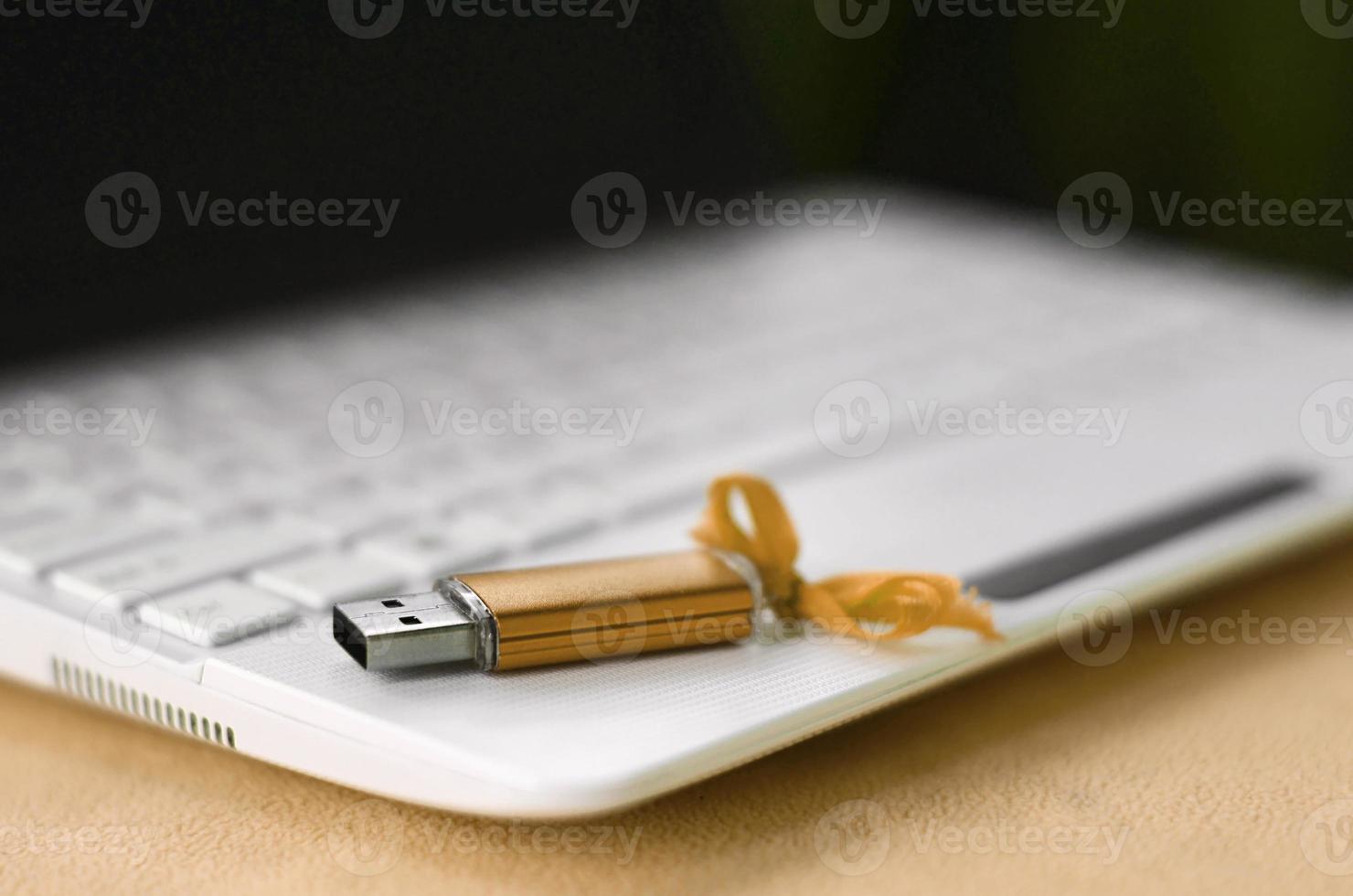 Orange usb flash memory card with a bow lies on a blanket of soft and furry light orange fleece fabric beside to a white laptop. Classic female gift design for a memory card photo