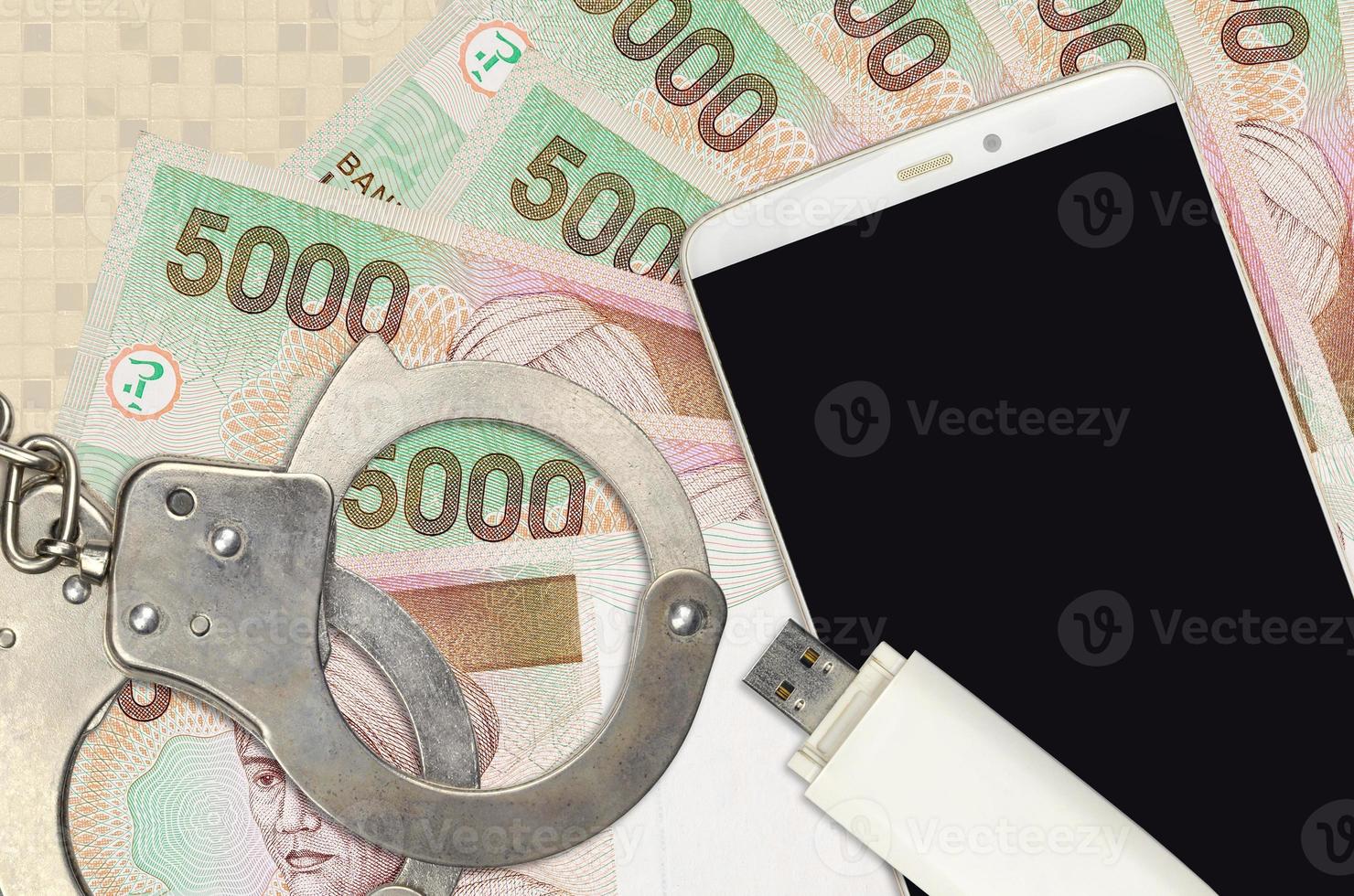 Billetes de 5000 rupias indonesias y smartphone con esposas policiales. concepto de ataques de phishing de piratas informáticos, estafa ilegal o distribución blanda de malware foto