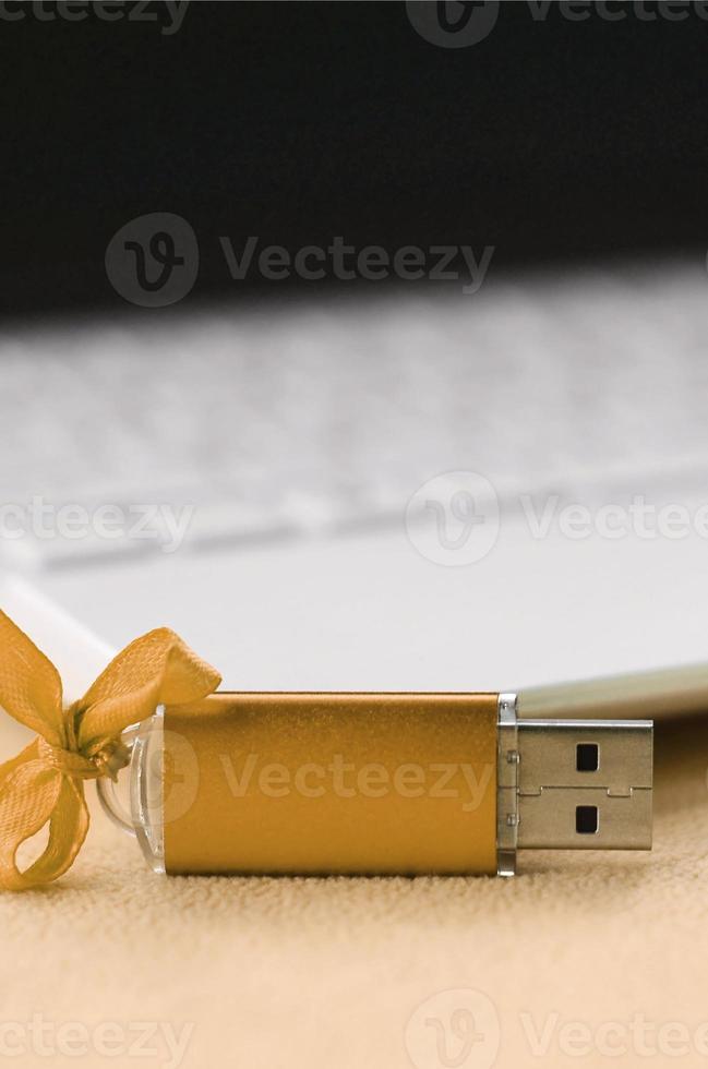 Orange usb flash memory card with a bow lies on a blanket of soft and furry light orange fleece fabric beside to a white laptop. Classic female gift design for a memory card photo