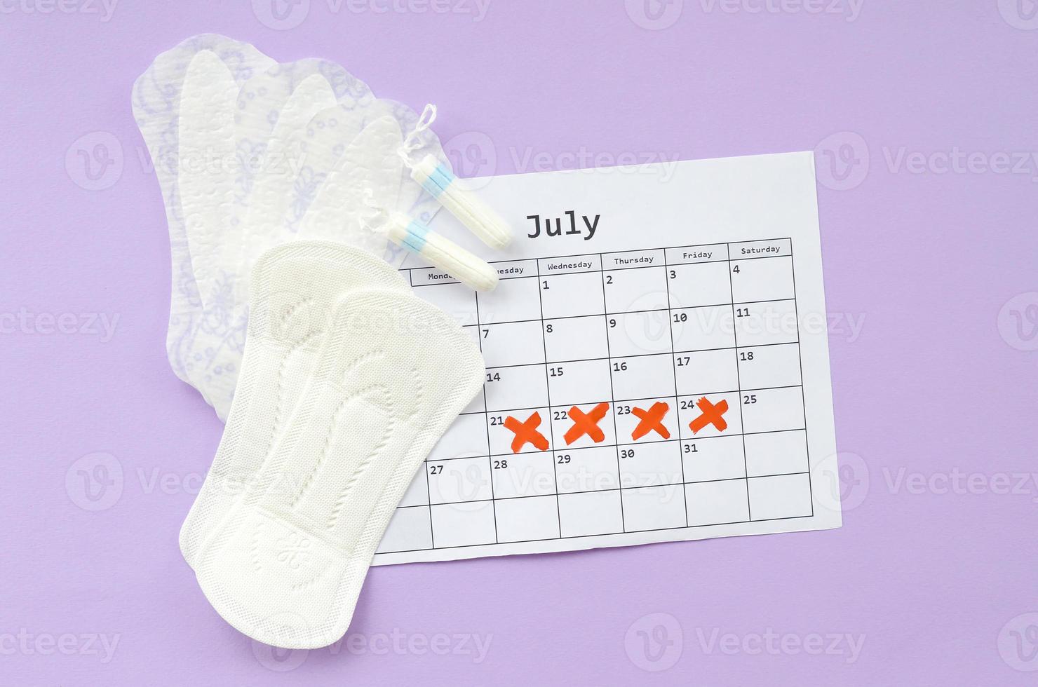 almohadillas menstruales y tampones en el calendario del período de menstruación sobre fondo lila foto