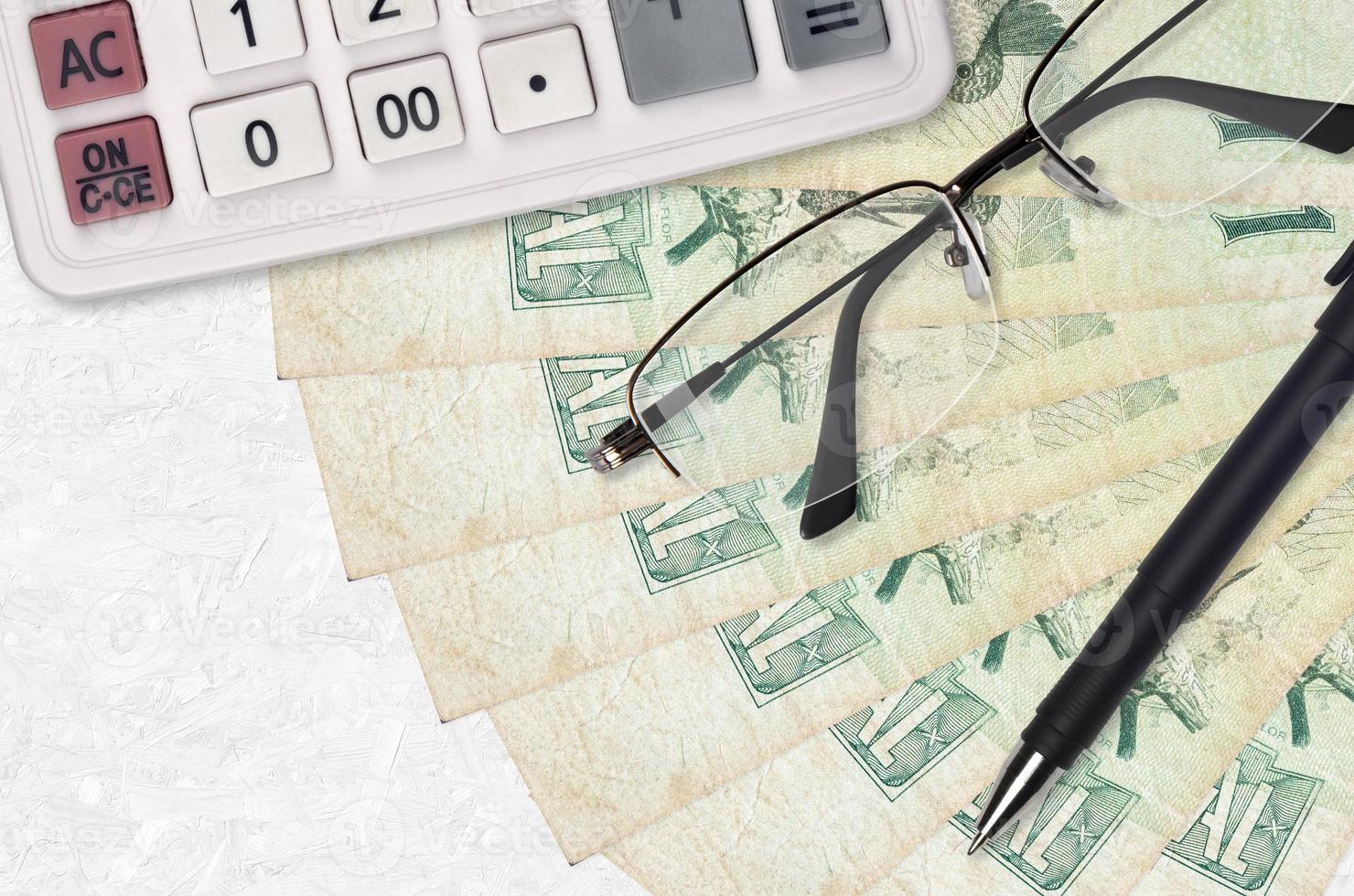 1 Brazilian real bills fan and calculator with glasses and pen. Business loan or tax payment season concept photo