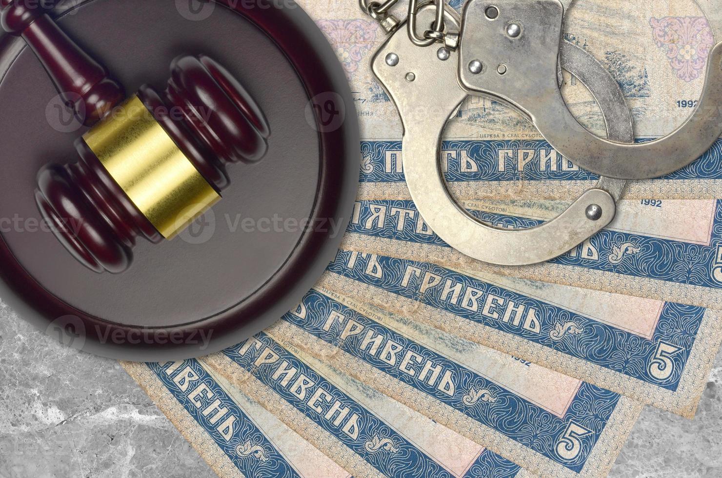 5 Ukrainian hryvnias bills and judge hammer with police handcuffs on court desk. Concept of judicial trial or bribery. Tax avoidance photo