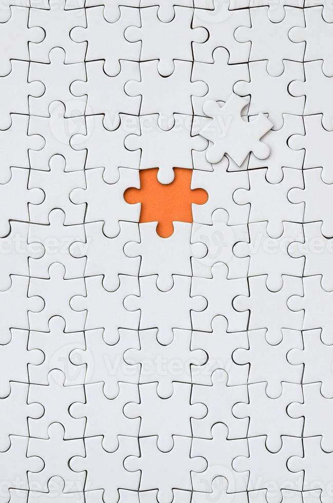 The texture of a white jigsaw puzzle in an assembled state with one missing element forming an orange space photo