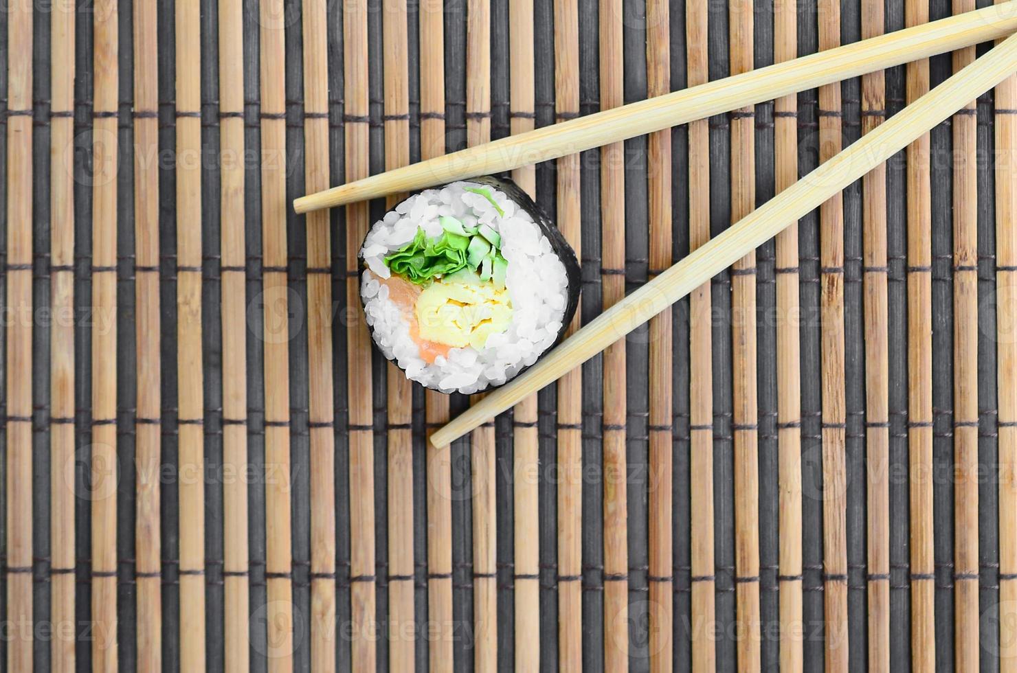 Sushi roll and wooden chopsticks lie on a bamboo straw serwing mat. Traditional Asian food. Top view. Flat lay minimalism shot with copy space photo
