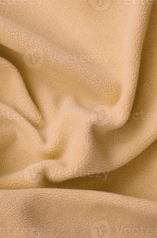 The blanket of furry orange fleece fabric. A background of light orange soft plush fleece material with a lot of relief folds photo