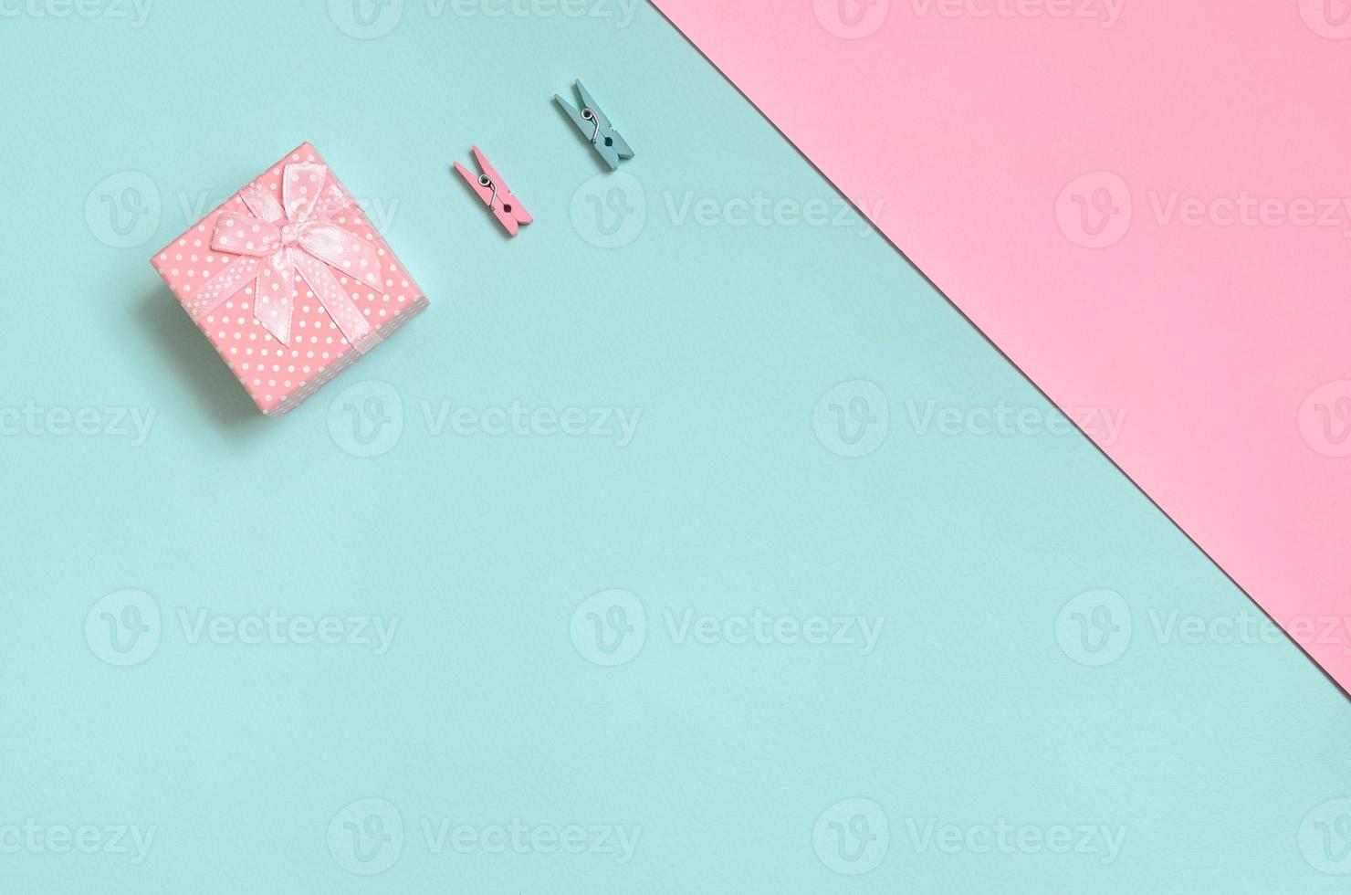 Small pink gift box and two pegs lie on texture background of fashion pastel blue and pink colors paper in minimal concept photo