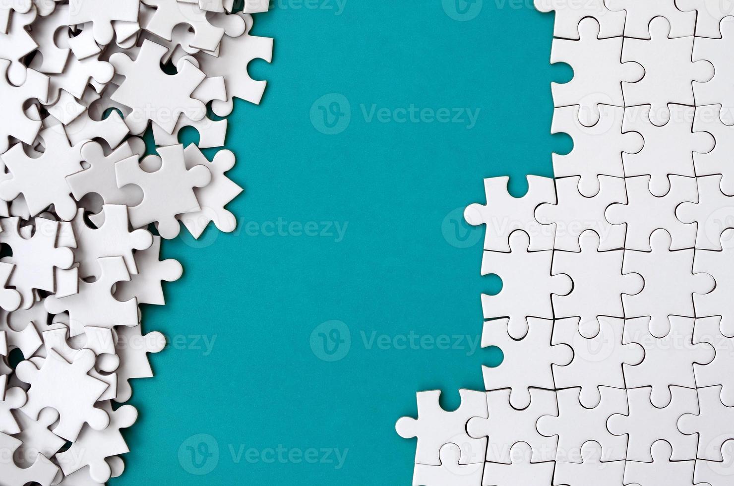 Fragment of a folded white jigsaw puzzle and a pile of uncombed puzzle elements against the background of a blue surface. Texture photo with space for text