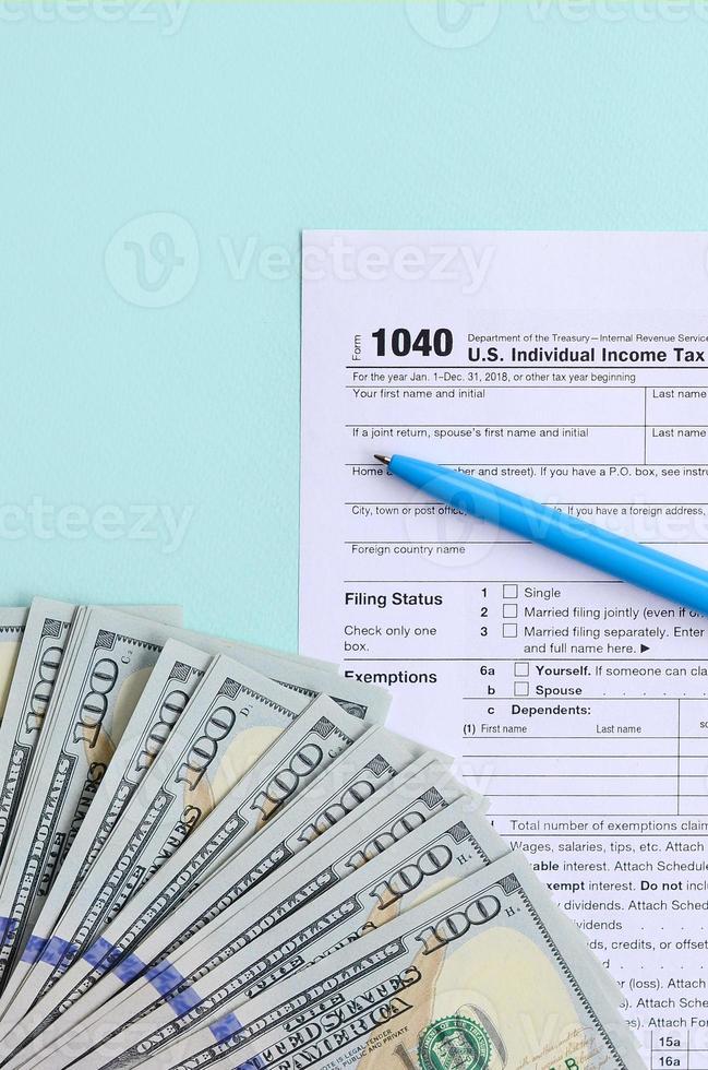 1040 tax form lies near hundred dollar bills and blue pen on a light blue background. US Individual income tax return photo