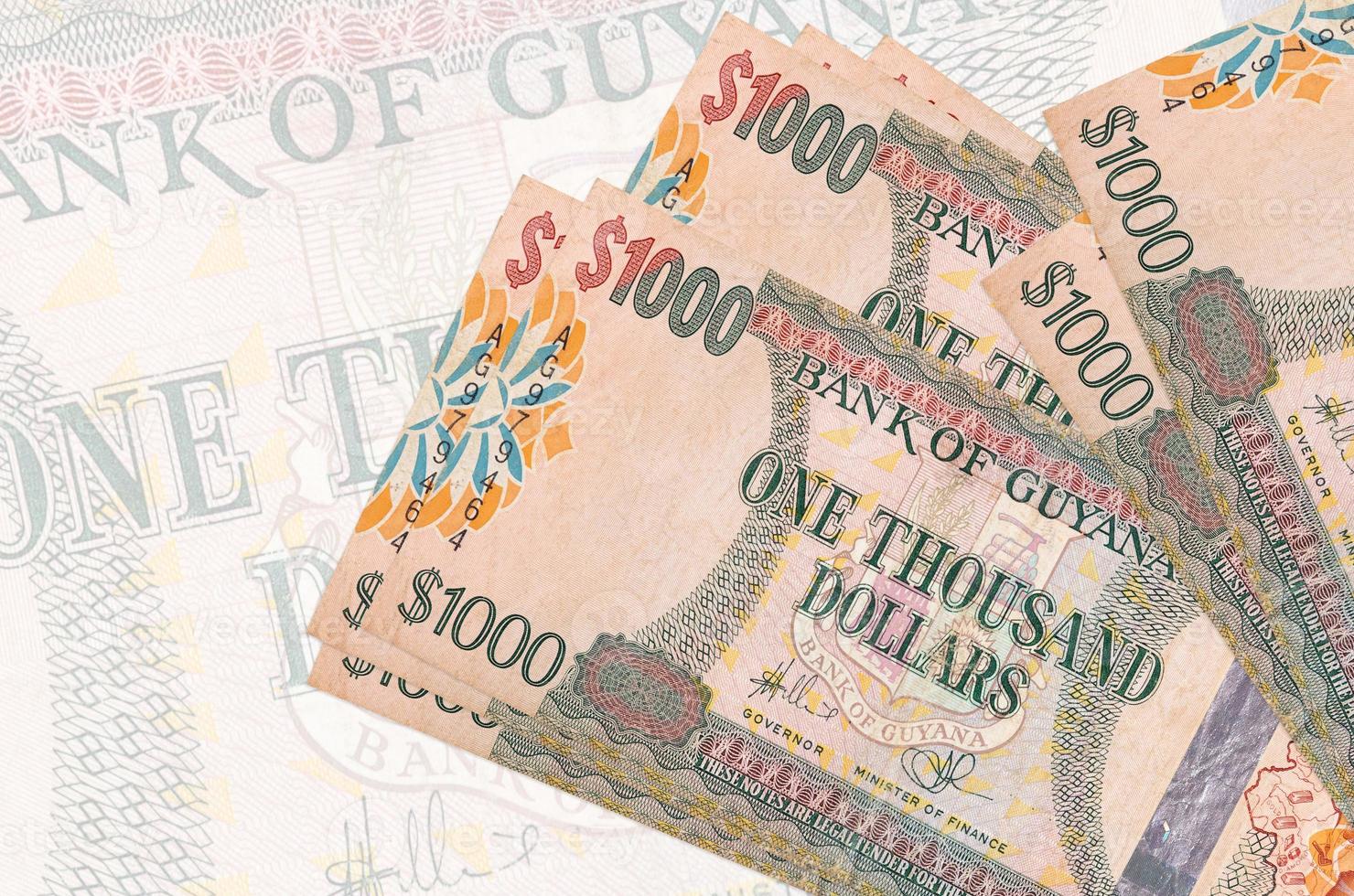 1000 Guyanese dollars bills lies in stack on background of big semi-transparent banknote. Abstract presentation of national currency photo