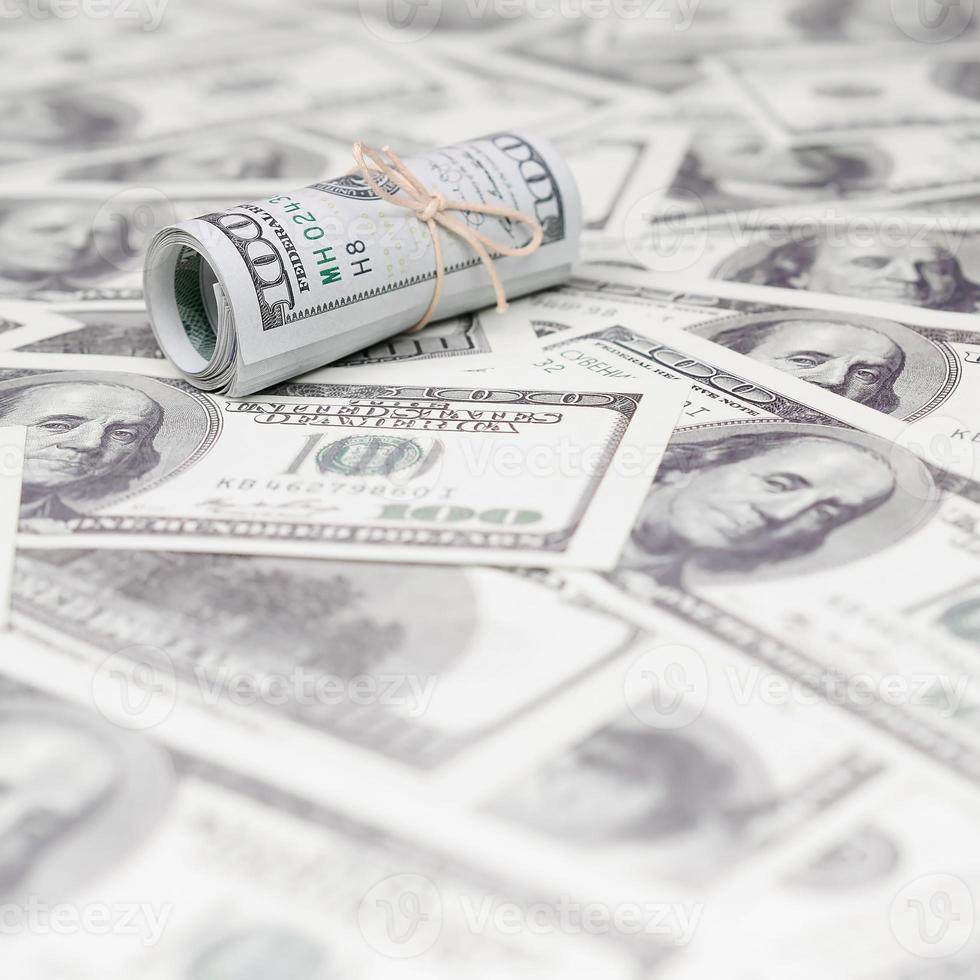 US dollars rolled up and tightened with band lies on a lot of american banknotes with blurred background photo