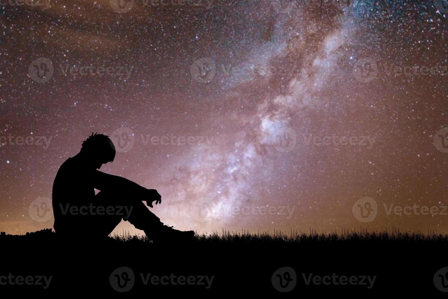 Loneliness, despair and regret concept. Lonely man in the meadow against the backdrop of stars and the Milky Way. photo