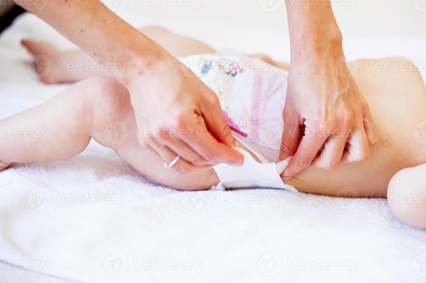 mother changing the diaper of her baby at home photo