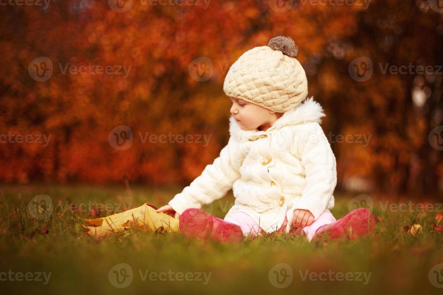 hermosa niñita sentada con una hoja grande en el parque de otoño foto