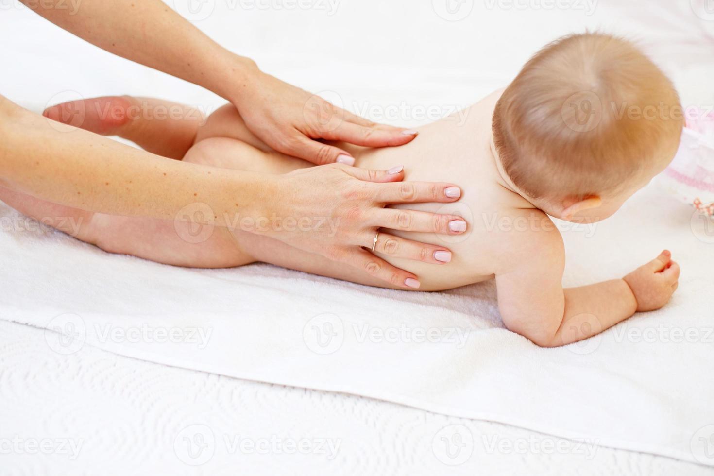 Mother massaging baby in bed at home photo
