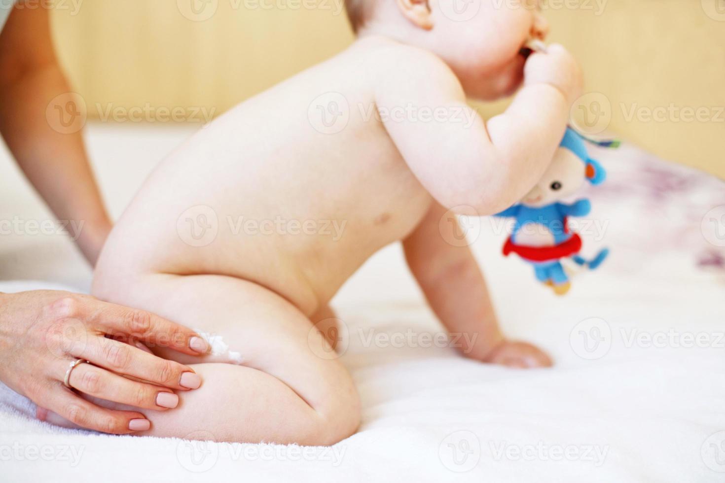 mother applying some cream by her hand to the baby ass for skin care. photo