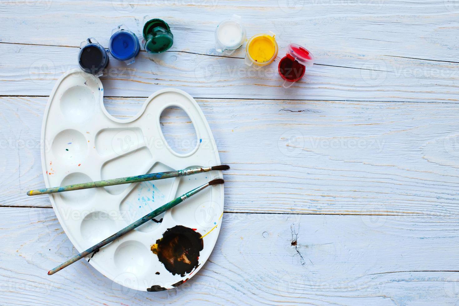 Paint palette with tassels and paints on a light blue wooden background. Flat lay art tools. Artwork workplace photo