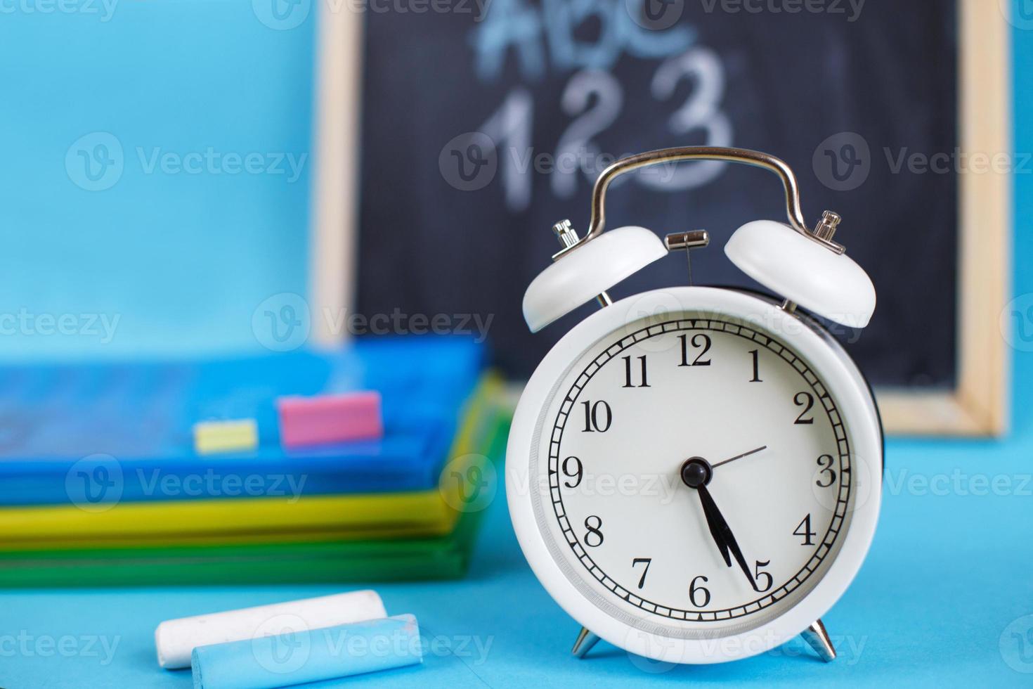 libros de texto y despertador con pizarra escolar sobre un fondo azul. De vuelta a la escuela. concepto de educación o negocios foto