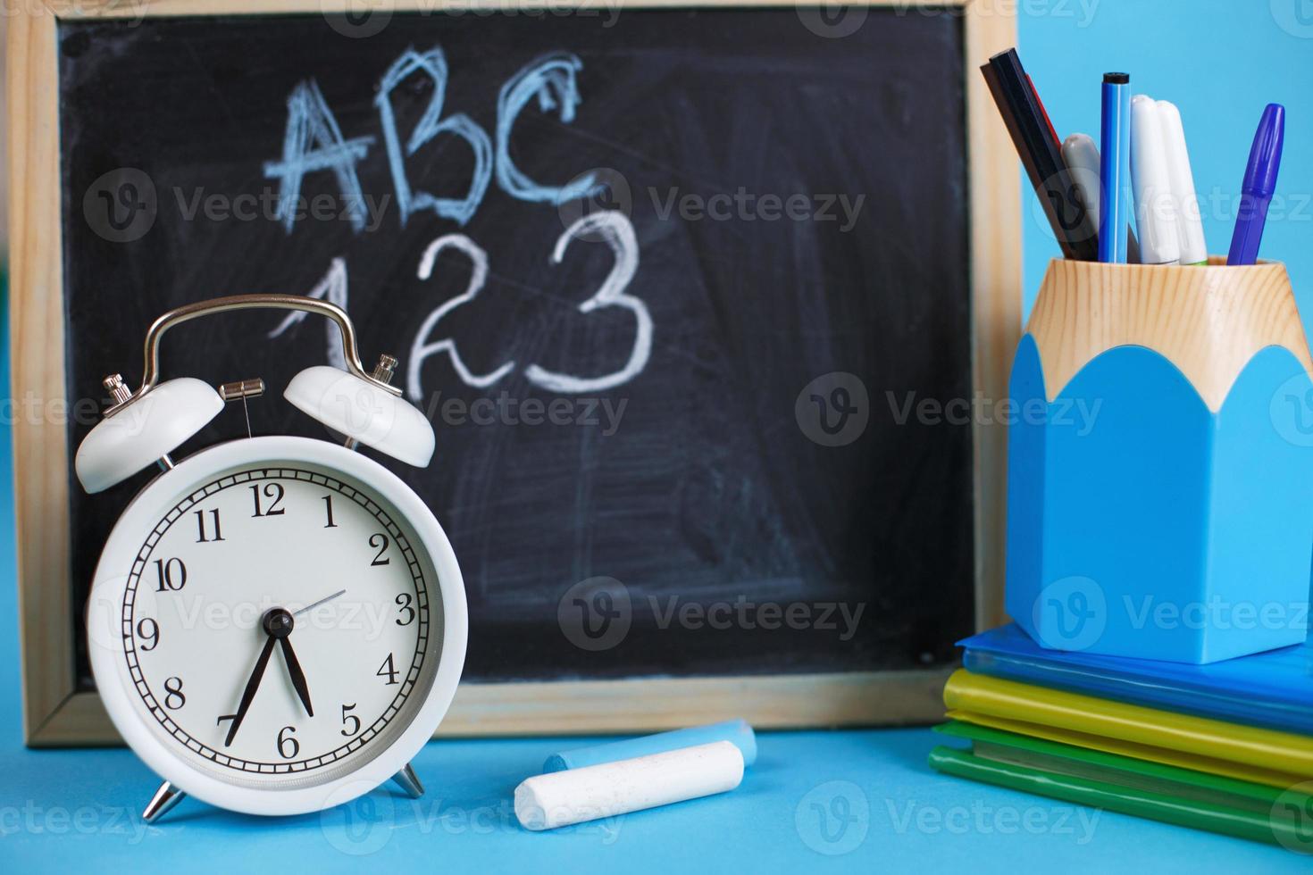 libros de texto y despertador con pizarra escolar sobre un fondo azul. De vuelta a la escuela. concepto de educación o negocios foto