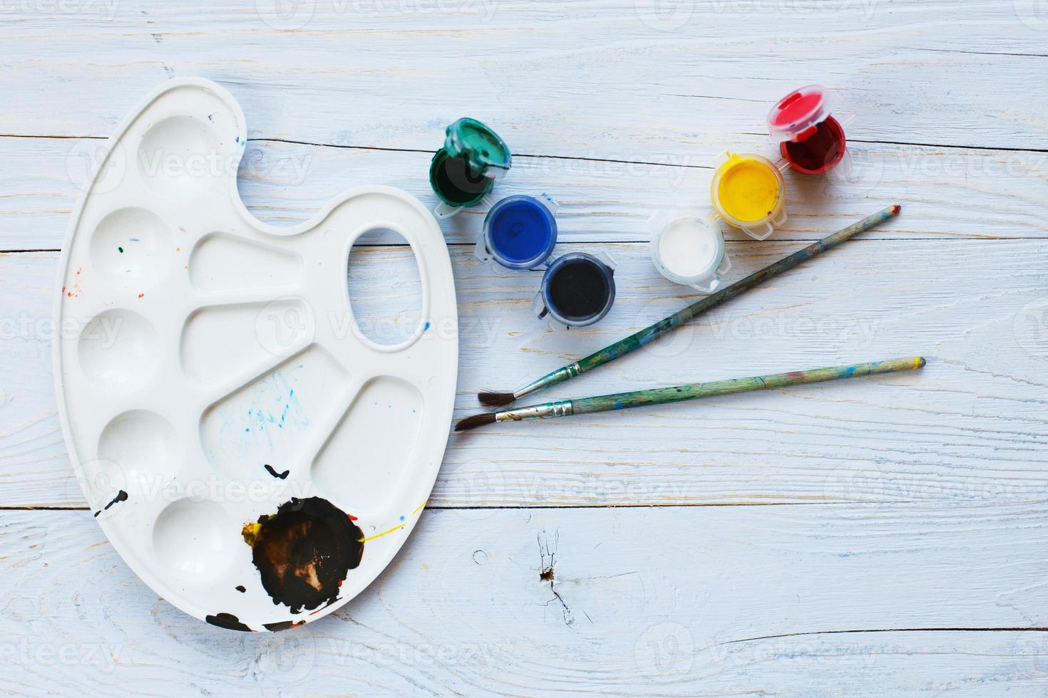 Paint palette with tassels and paints on a light blue wooden background. Flat lay art tools. Artwork workplace photo