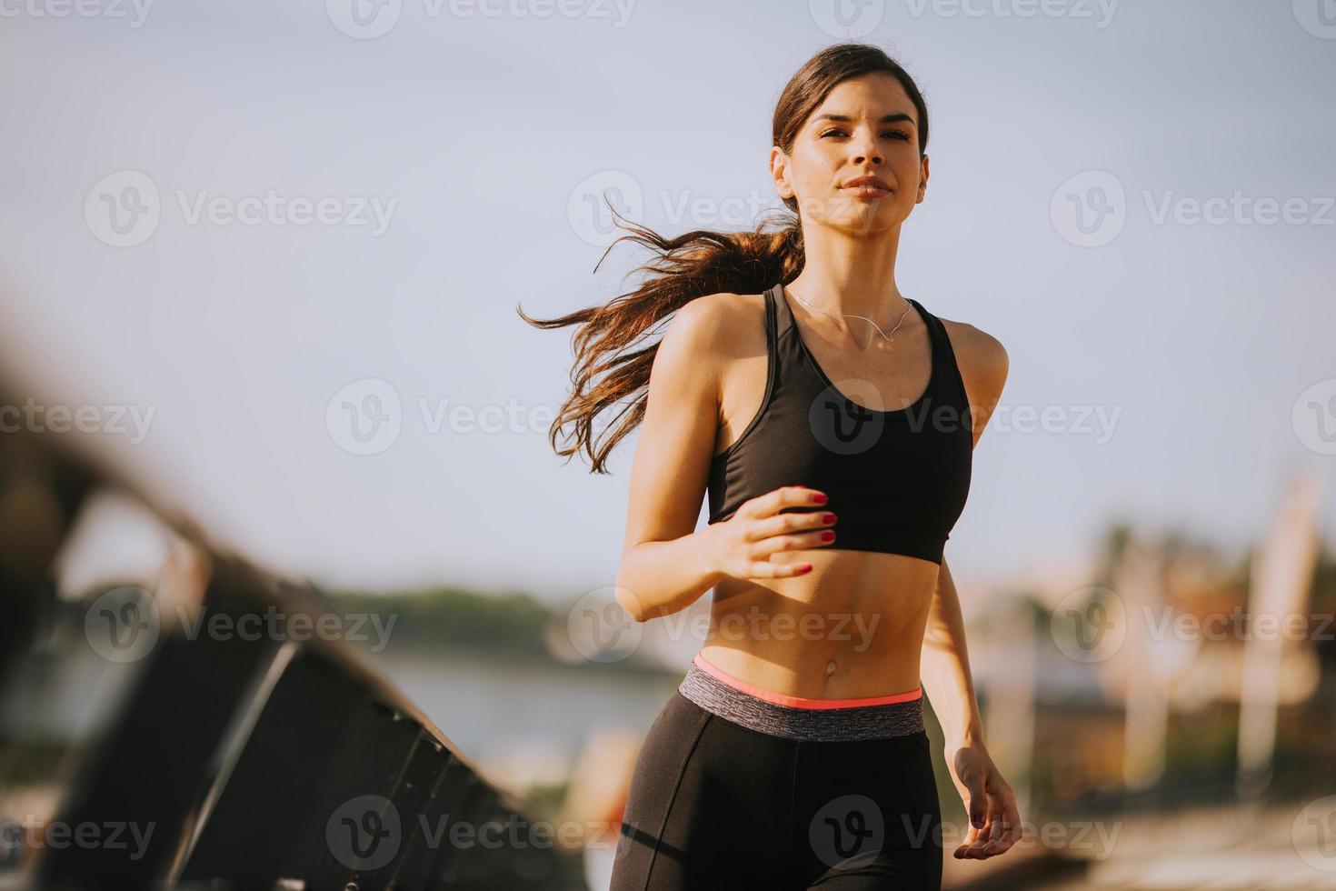 hermosa mujer joven activa corriendo en el paseo marítimo a lo largo de la orilla del río foto