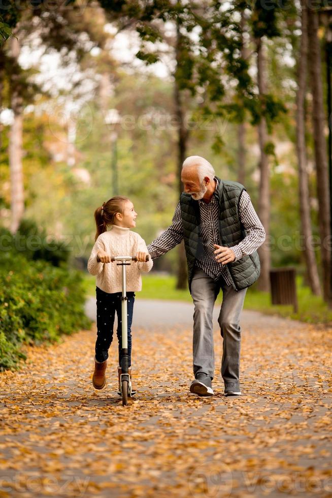 un anciano enseñando a su nieta a andar en patinete en el parque foto
