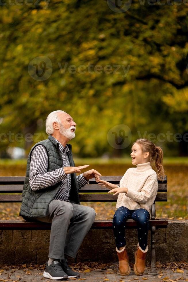 Grandfather playing red hands slapping game with his granddaughter in park on autumn day photo