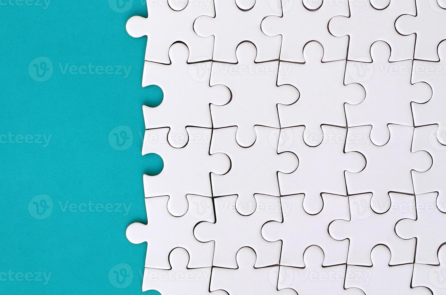 Fragment of a folded white jigsaw puzzle on the background of a blue plastic surface. Texture photo with copy space for text