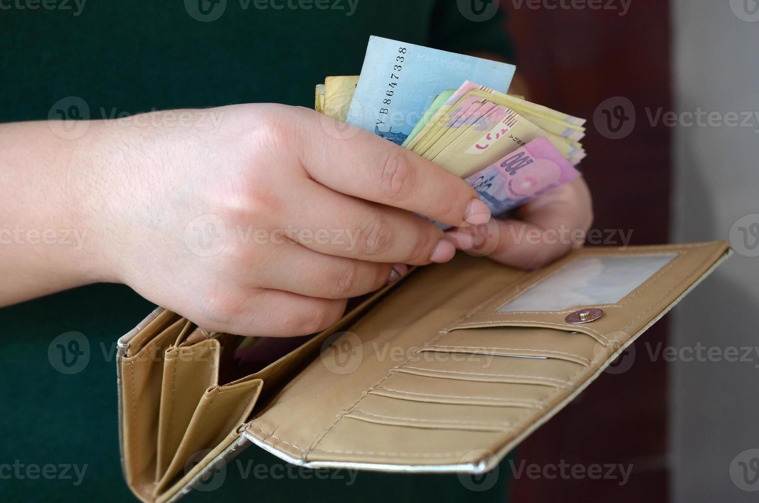 manos femeninas sosteniendo billetes de hryvnia ucraniana en una pequeña bolsa de dinero o billetera foto