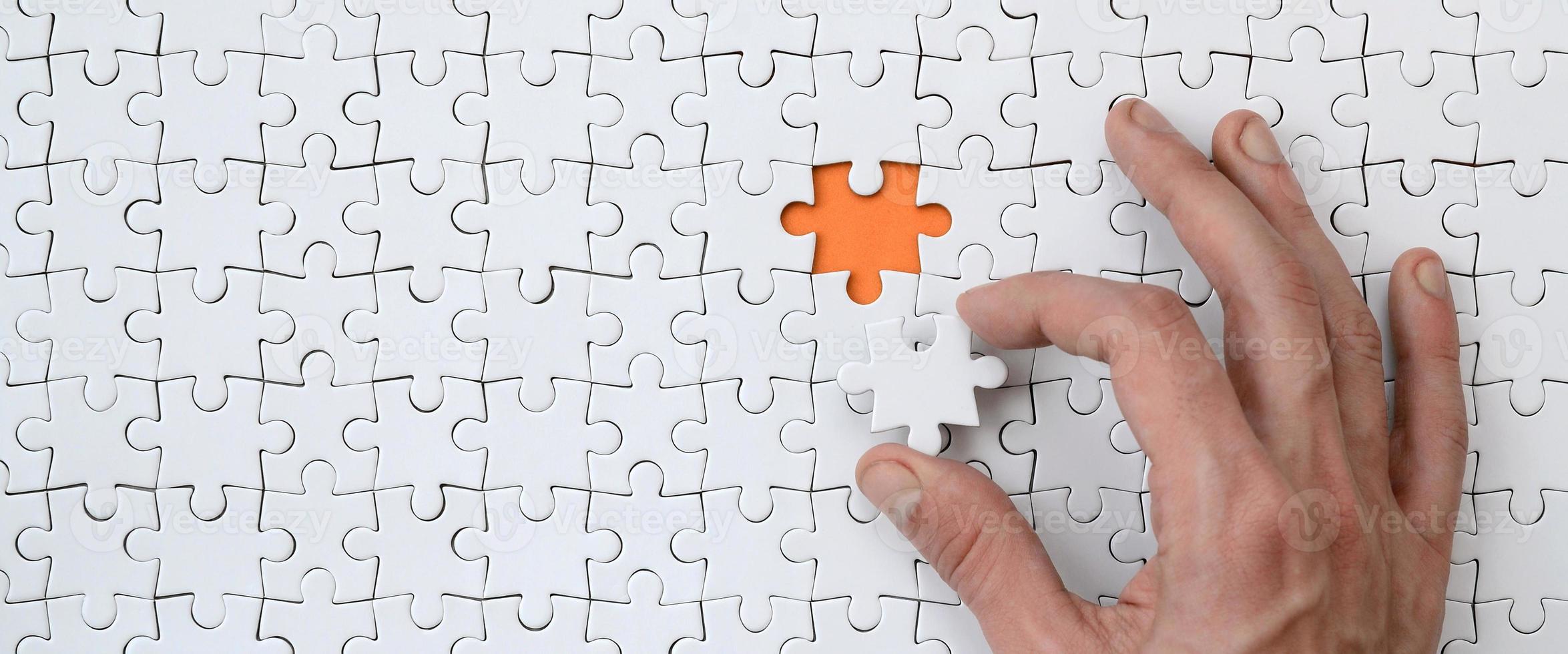 The texture of a white jigsaw puzzle in the assembled state with one missing element that the male hand puts in photo