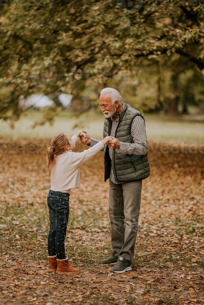 Grandfather spending time with his granddaughter in park on autumn day photo