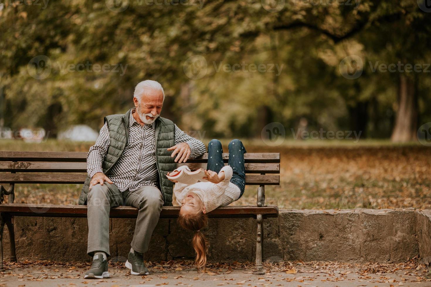 Grandfather spending time with his granddaughter on bench in park on autumn day photo