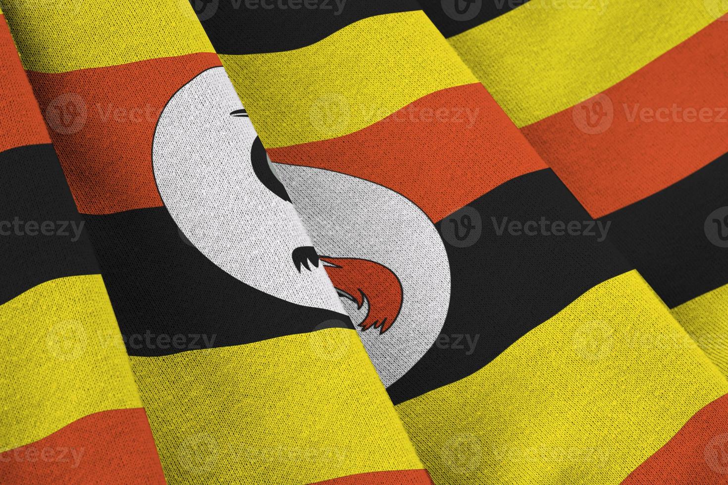 Uganda flag with big folds waving close up under the studio light indoors. The official symbols and colors in banner photo