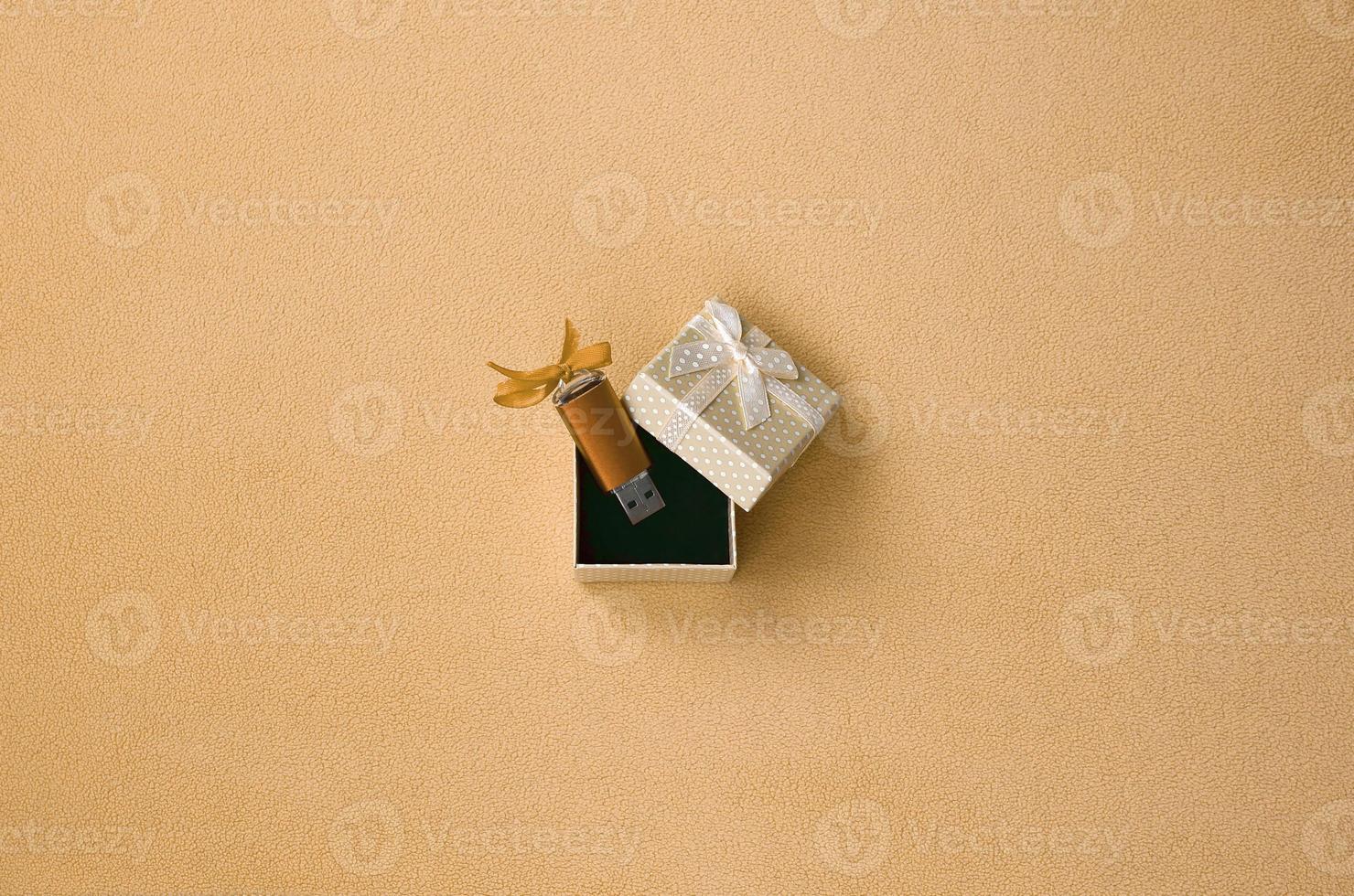 Orange usb flash memory card with a bow lies in a small gift box with a small bow on a blanket of soft and furry light orange fleece fabric. Classic fashion gift memory card design photo