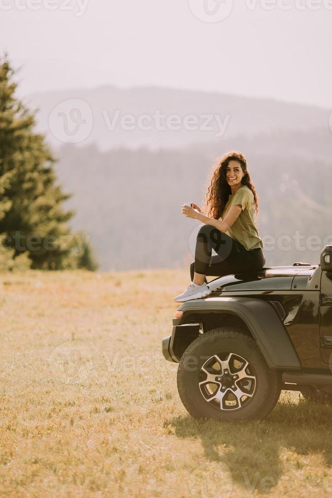 mujer joven relajándose en el capó de un vehículo de terreno en el campo foto