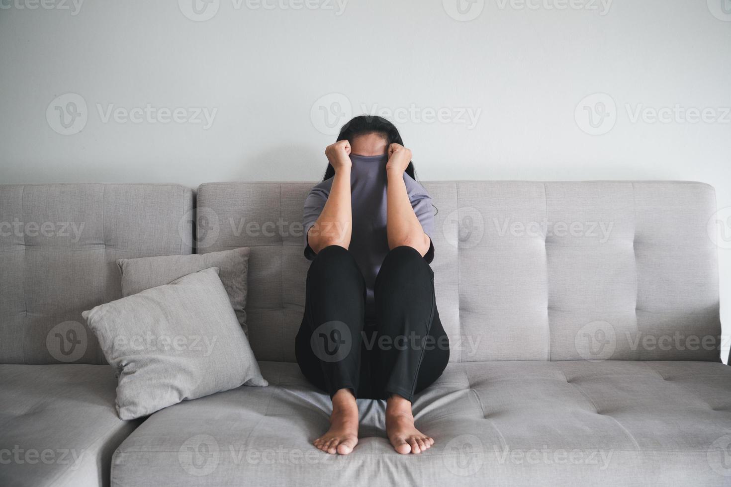 Schizophrenia with lonely and sad in mental health depression concept. Depressed woman sitting against on the sofa at home with dark room feeling miserable. Women are depressed, fearful and unhappy. photo