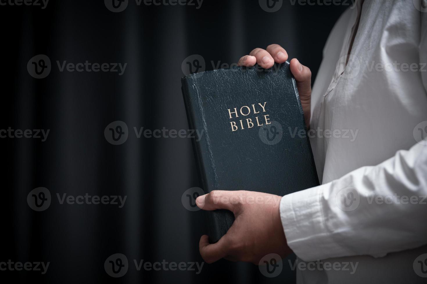 Faith with holy bible concept. Hands of a female prayer worship God with holy bible on black background in church. Christian woman who believe in Jesus read and study the grace of the holy scriptures. photo