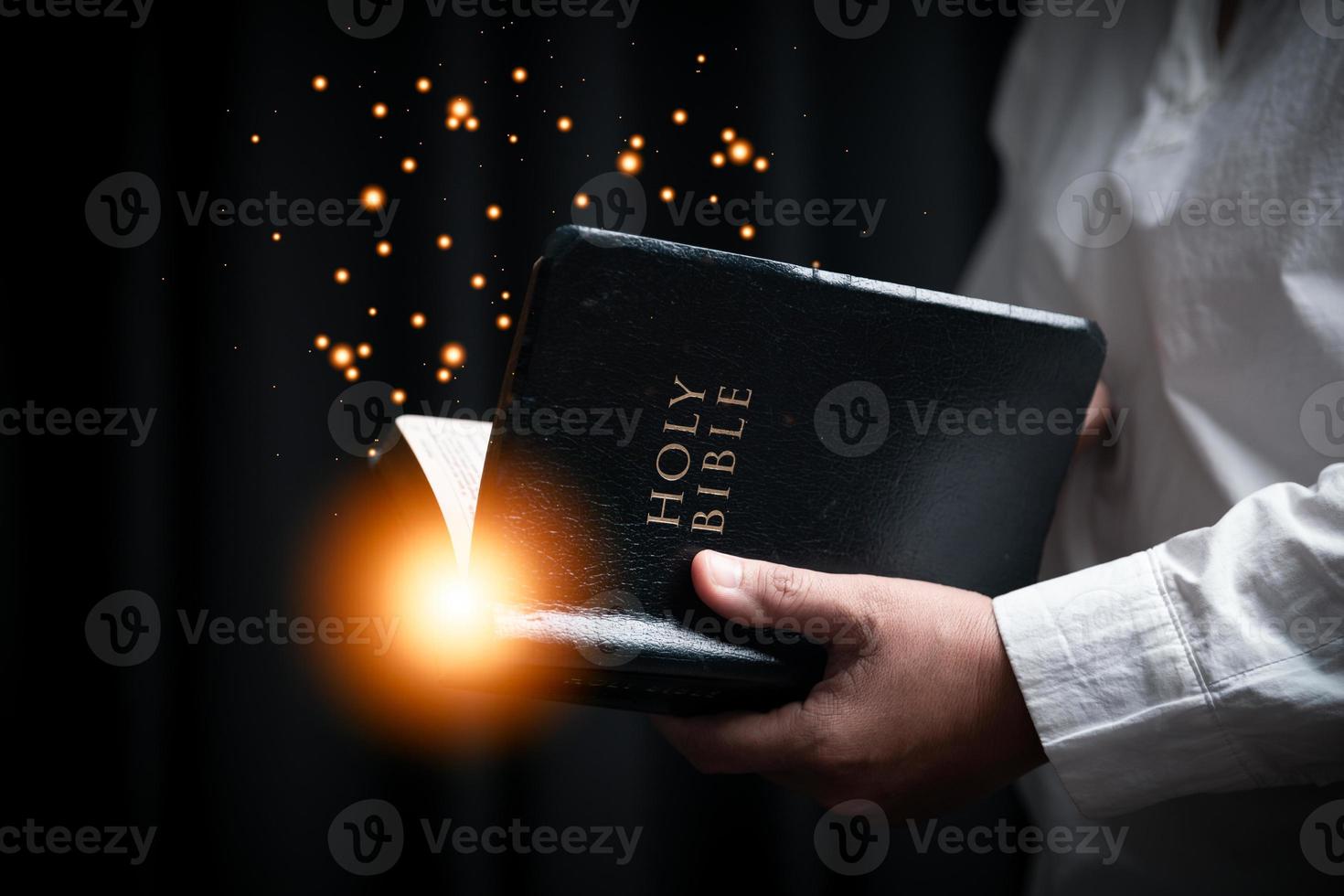 Faith with holy bible concept. Hands of a female prayer worship God with holy bible on black background in church. Christian woman who believe in Jesus read and study the grace of the holy scriptures. photo