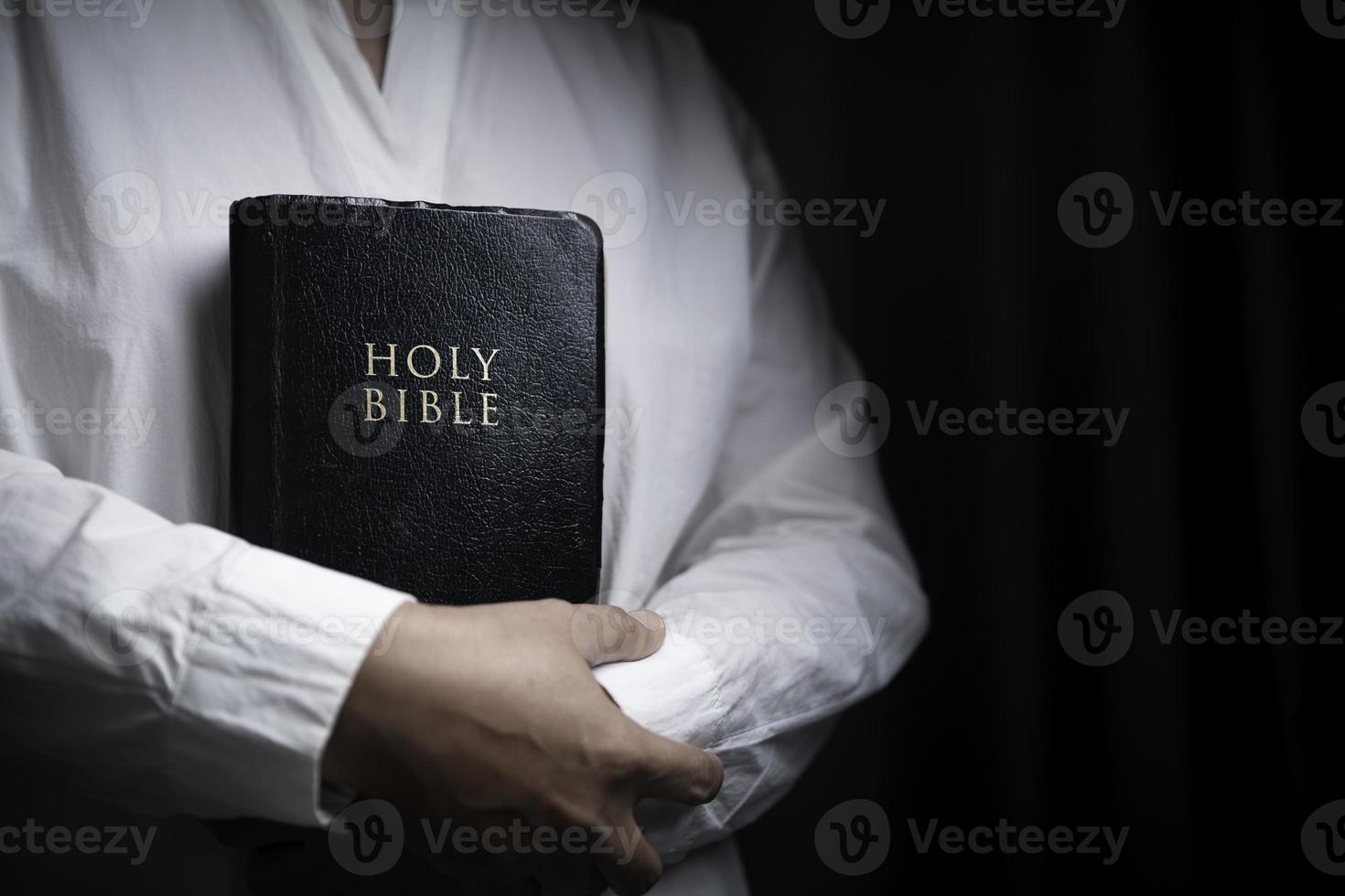 Faith with holy bible concept. Hands of a female prayer worship God with holy bible on black background in church. Christian woman who believe in Jesus read and study the grace of the holy scriptures. photo