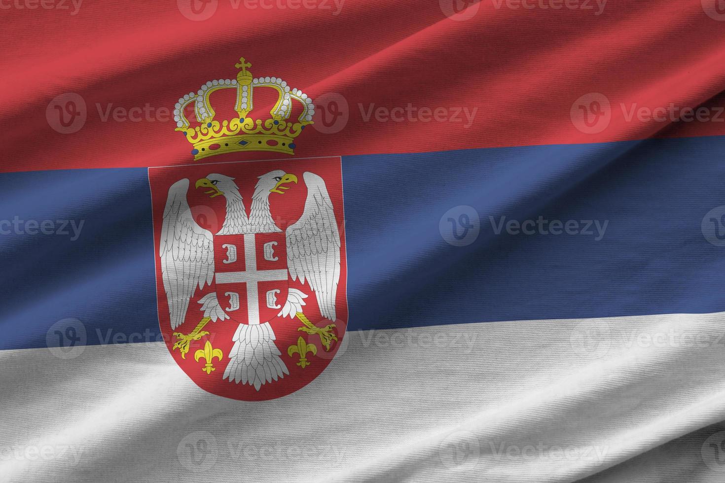 Serbia flag with big folds waving close up under the studio light indoors. The official symbols and colors in banner photo