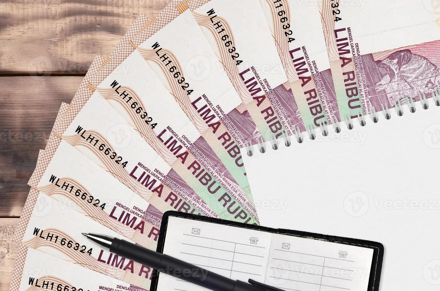 Ventilador de billetes de 5000 rupias indonesias y bloc de notas con libreta de contactos y bolígrafo negro. concepto de planificación financiera y estrategia empresarial foto