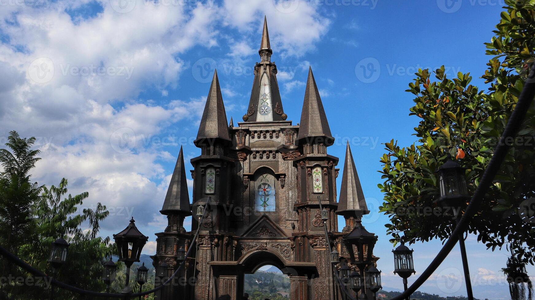 Miniature castle with medieval exterior soaring into the sky with blue clouds and trees on the left and right. photo