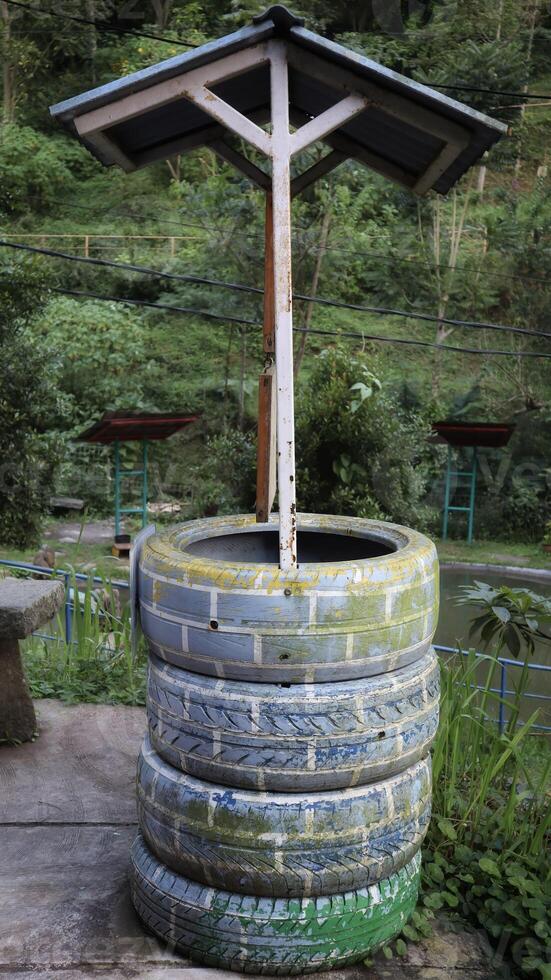 Four tires were stacked and then painted like a brick pattern and installed a roof resembling an old well, used as decorations for parks and parks. photo