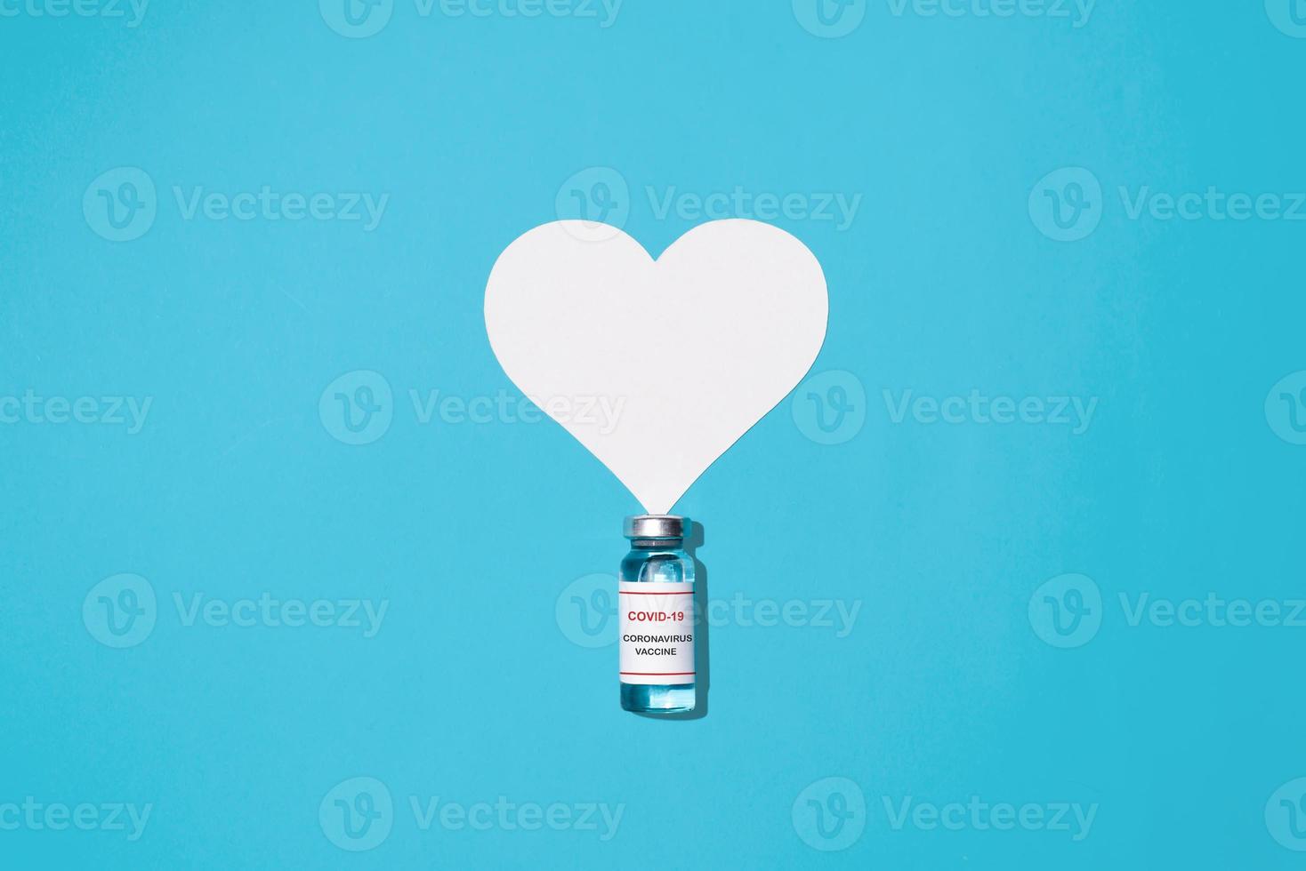 Vial of COVID-19 vaccine and heart on a blue background, flat lay. Global population vaccination, healthcare and medicine concept. photo