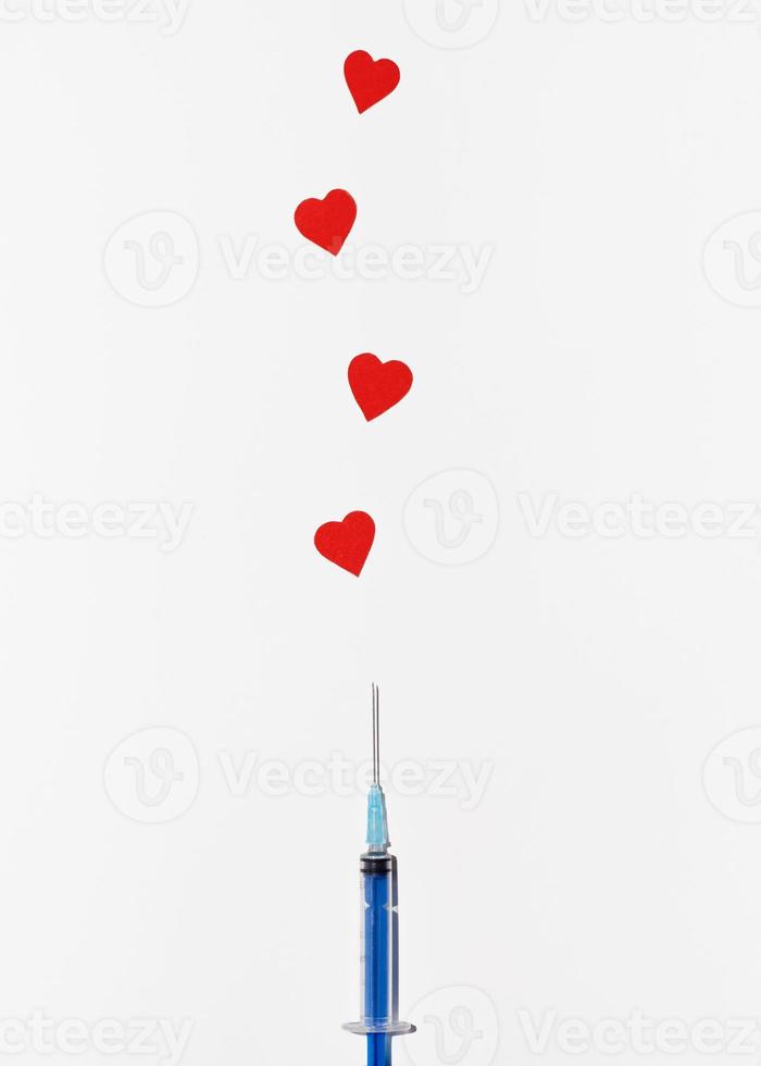 Creative symbol of safe worldwide vaccination. Syringe injecting hearts on white background, top view photo