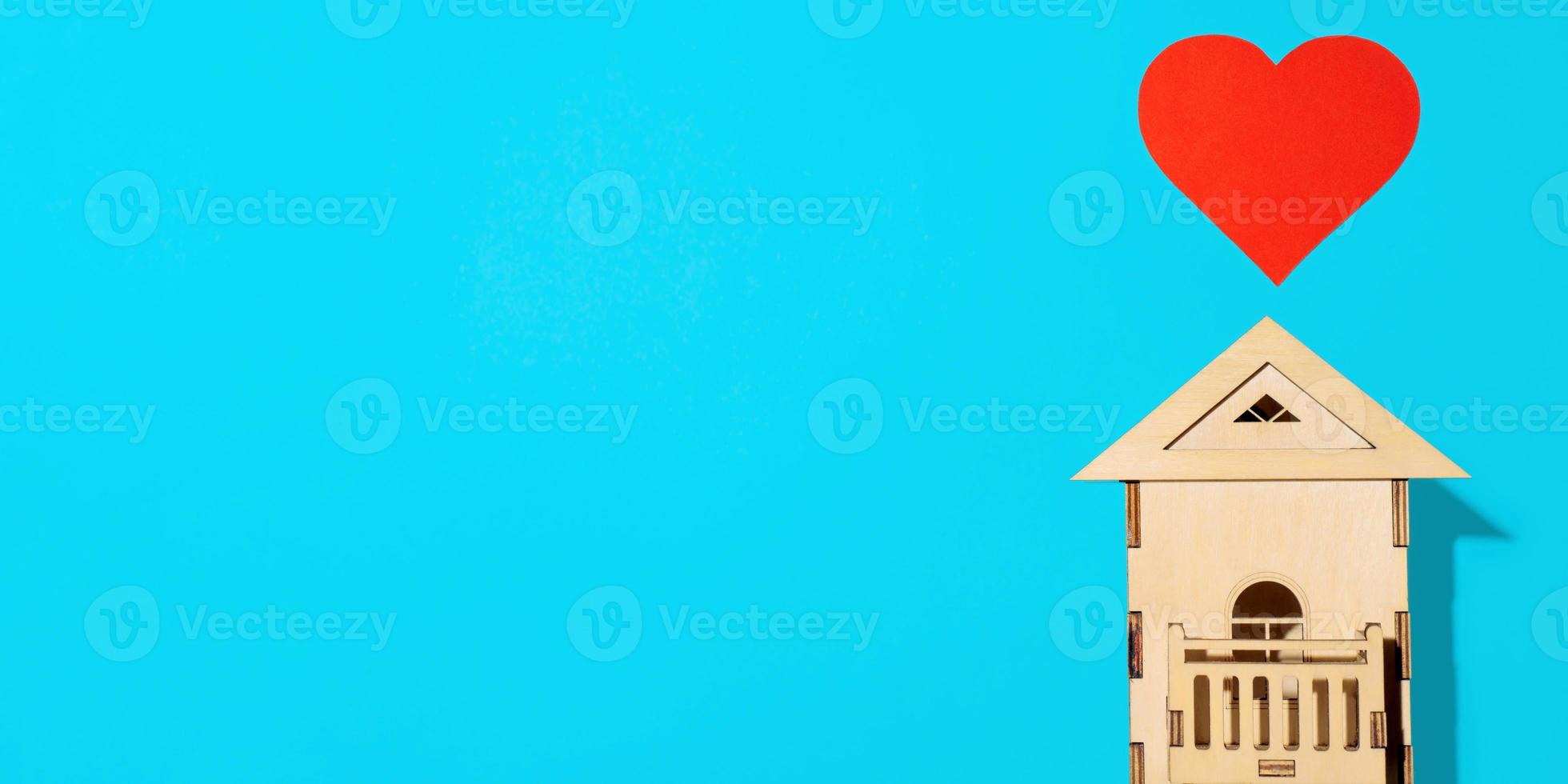 Wooden model of house and red paper heart on light blue background, flat lay. Home Sweet Home. Conceptual banner top view, copy space. photo