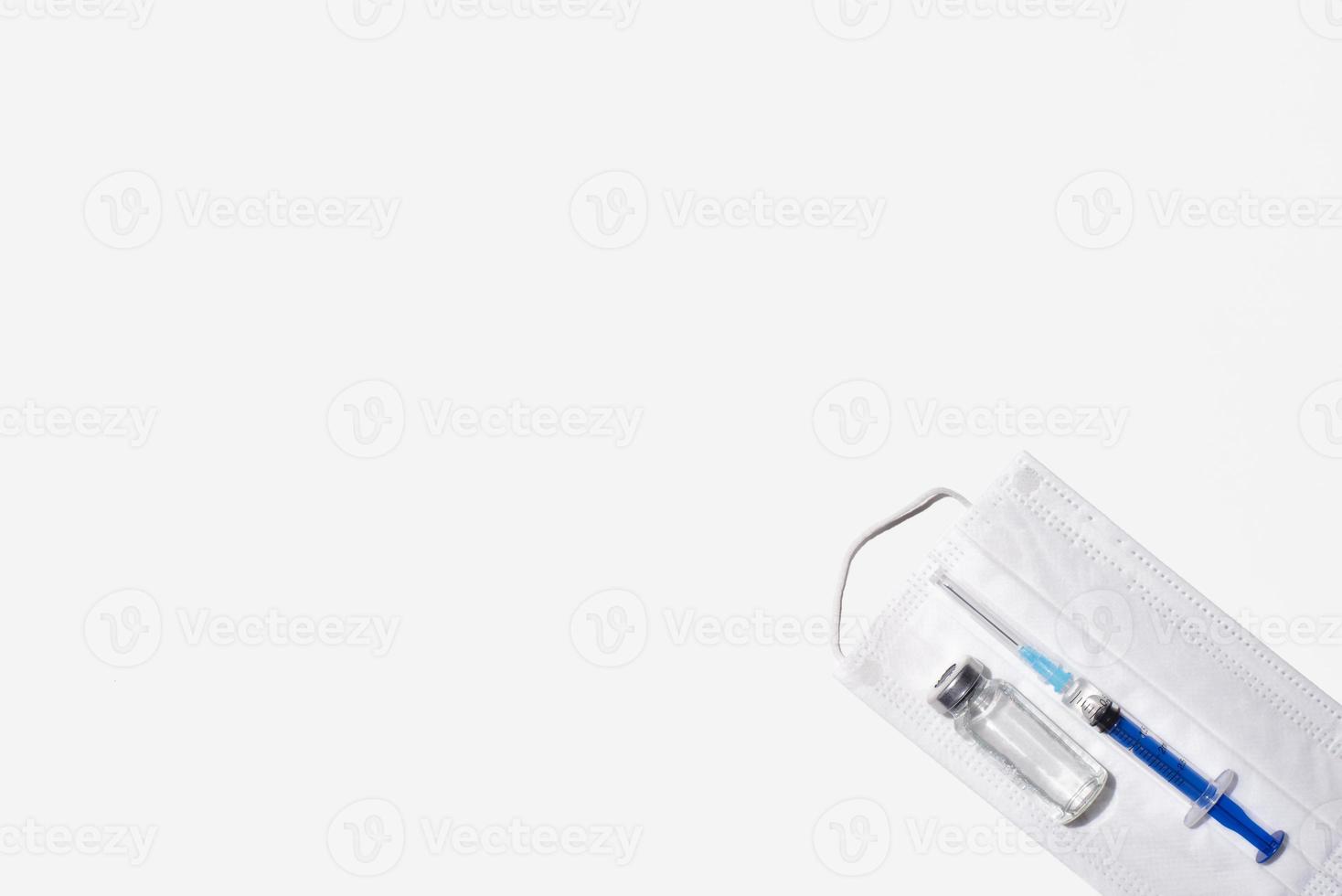 Disease vaccination equipment, copy space. Ampoule, medical face mask and syringe on a white background, flat lay. photo