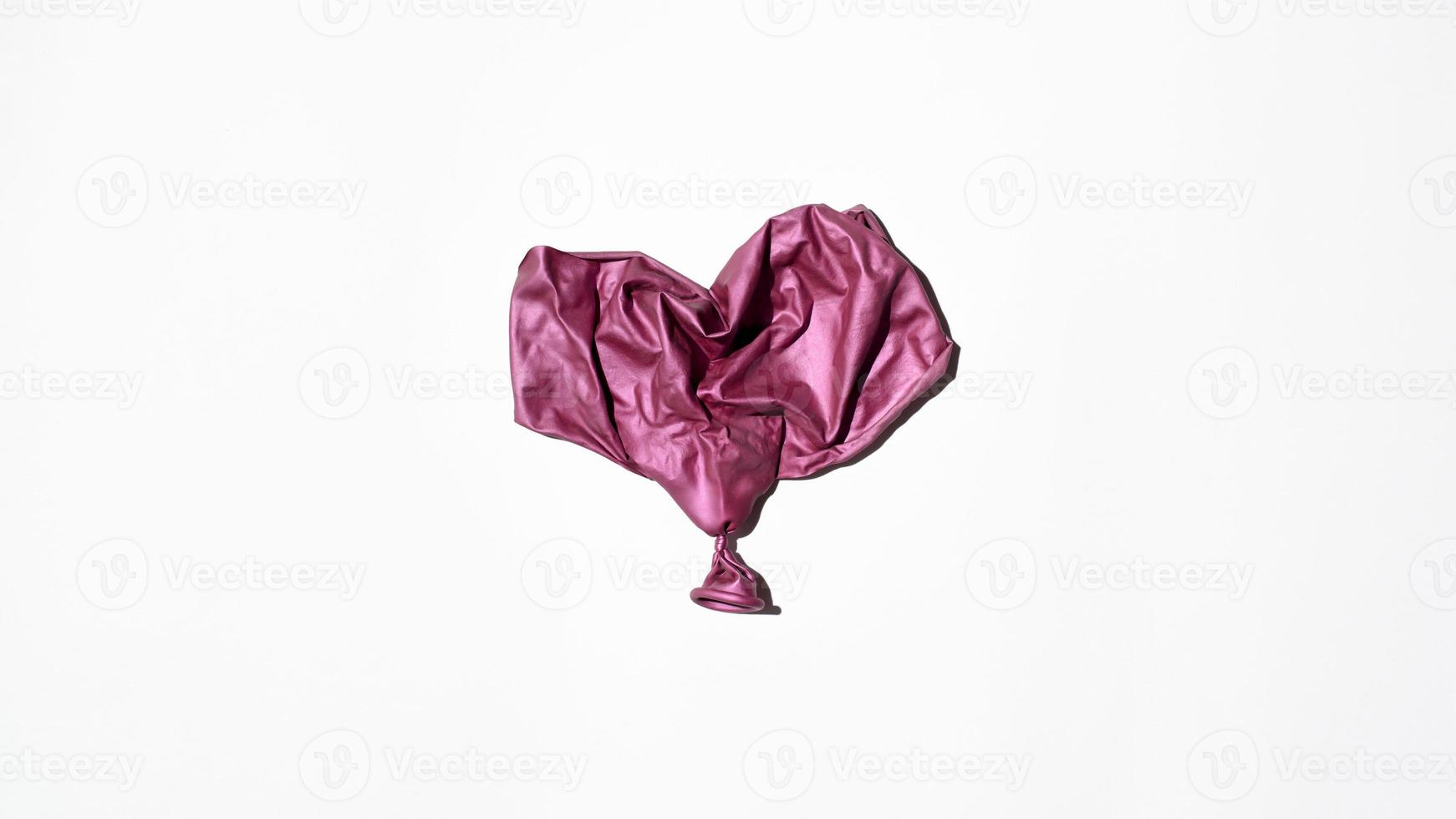 Burst balloon in the shape of a heart on a white background, top view photo