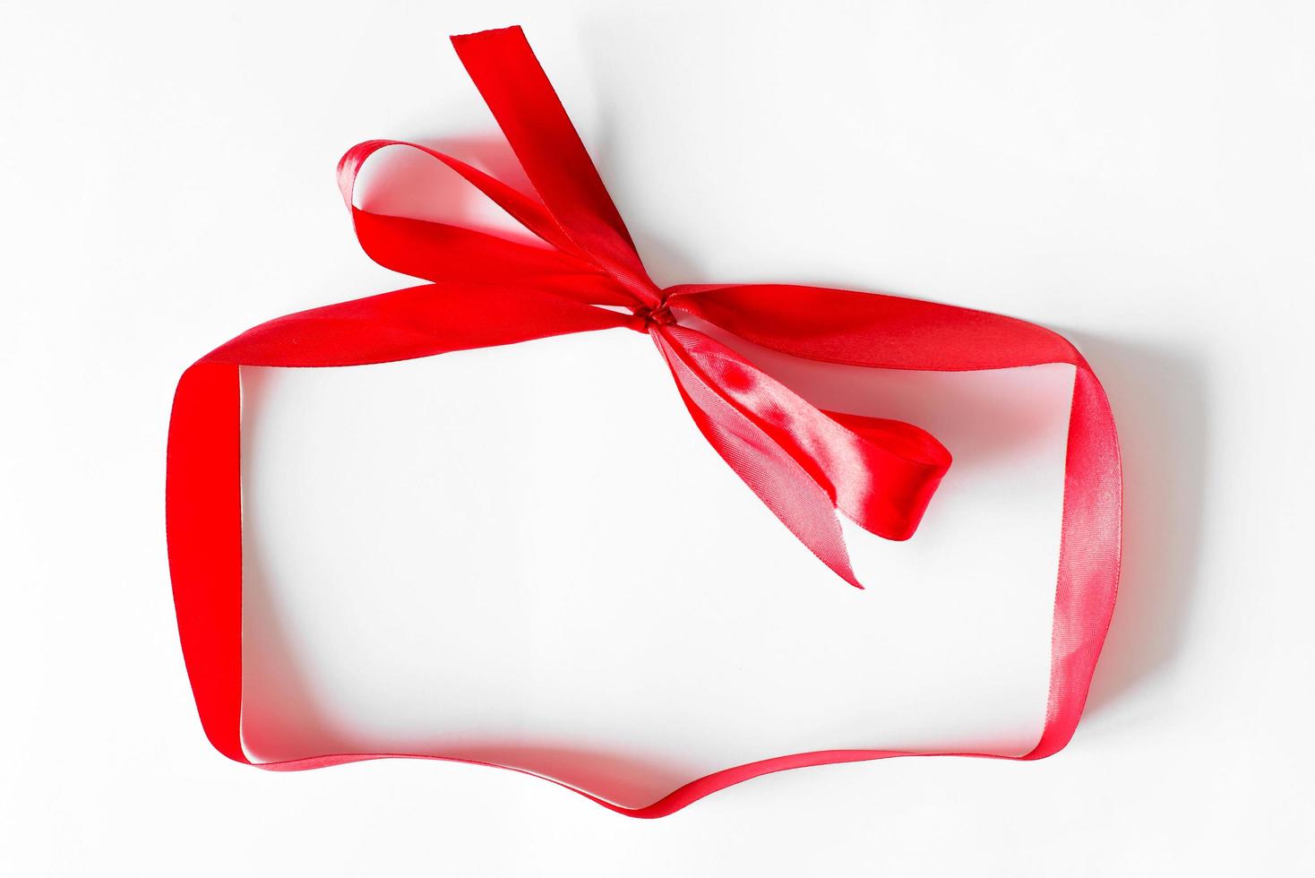 Red ribbon with bow shaped gift box on white background with place for text inside. Top view, copy space photo