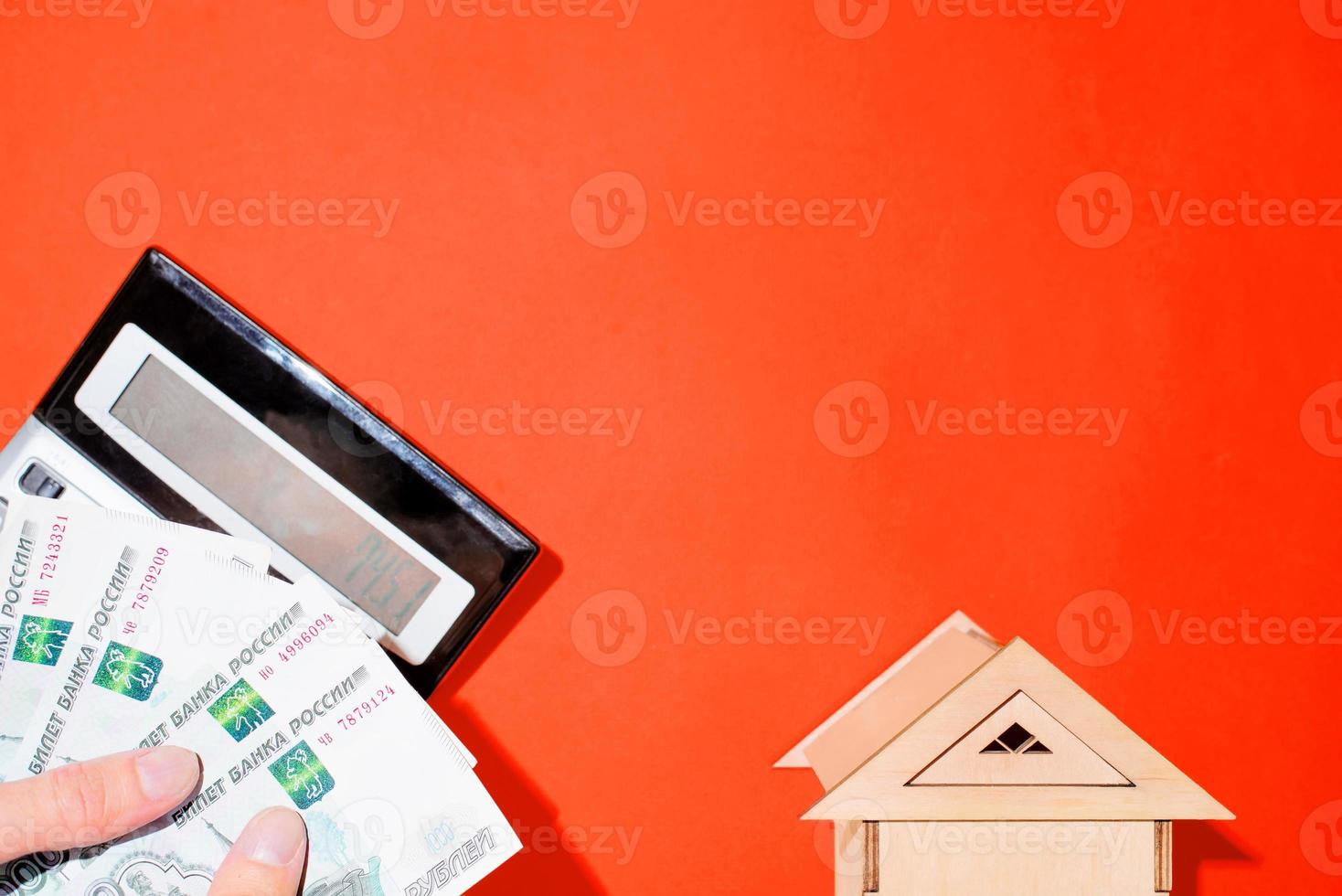 Man's hands counting money, calculator and a toy house. Red background top view, place for text. Calculation of personal finances, payment of utilities photo